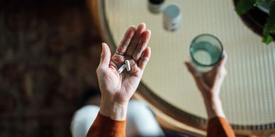 Person holding two white pills and a glass of water, preparing to take medication.