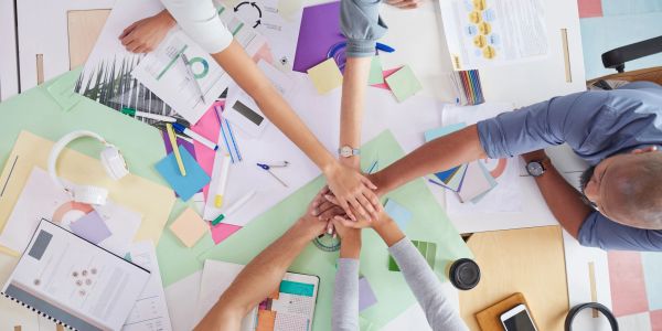 Teamwork with hands joined over a busy desk.
