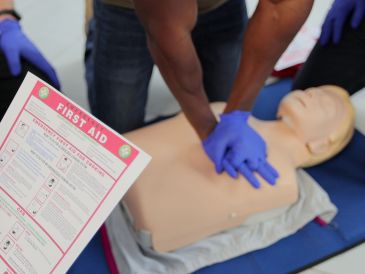 Person practicing CPR on a dummy with first aid instructions.