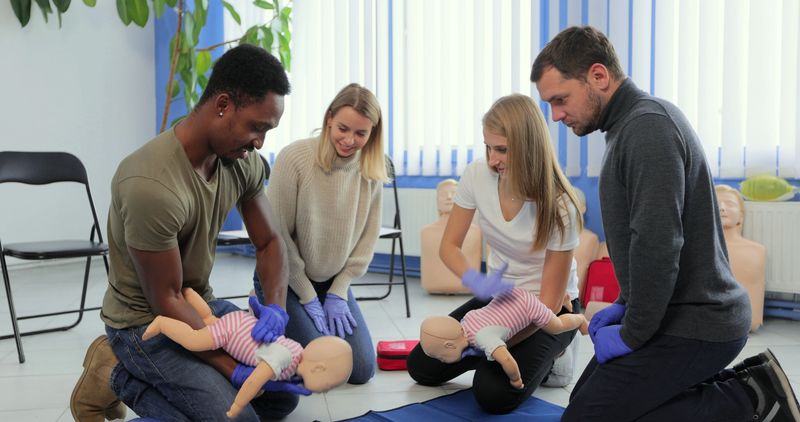 Group of multiethnic people during the first aid training with instructor showing on manikin how to do artificial respiration for the baby