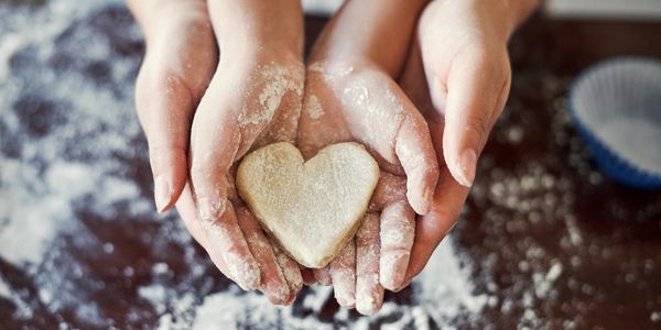 Two hands holding heart-shaped cookie dough covered in flour.