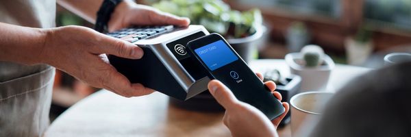 Person making a contactless payment using a mobile phone at a cafe.