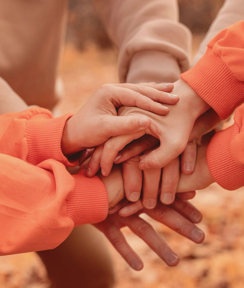 Hands of people folded one on top of the other on a yellow background. Family support, support, brotherhood.