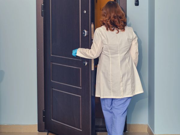A medical professional opening a door, wearing gloves and scrubs.