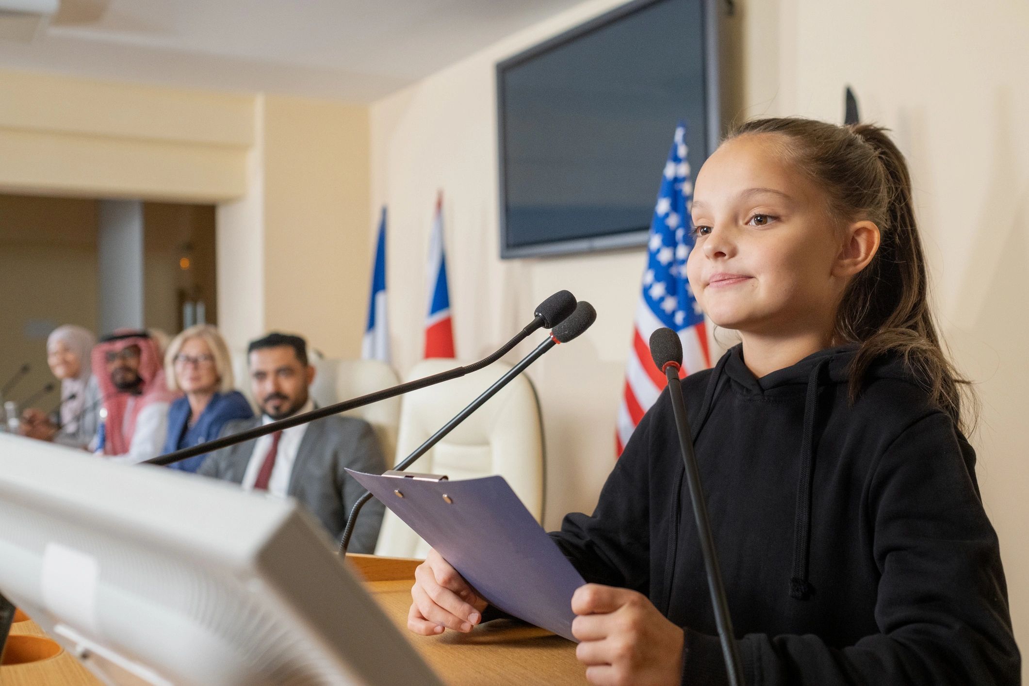 Young girl speaking at a conference with a diverse panel behind her.