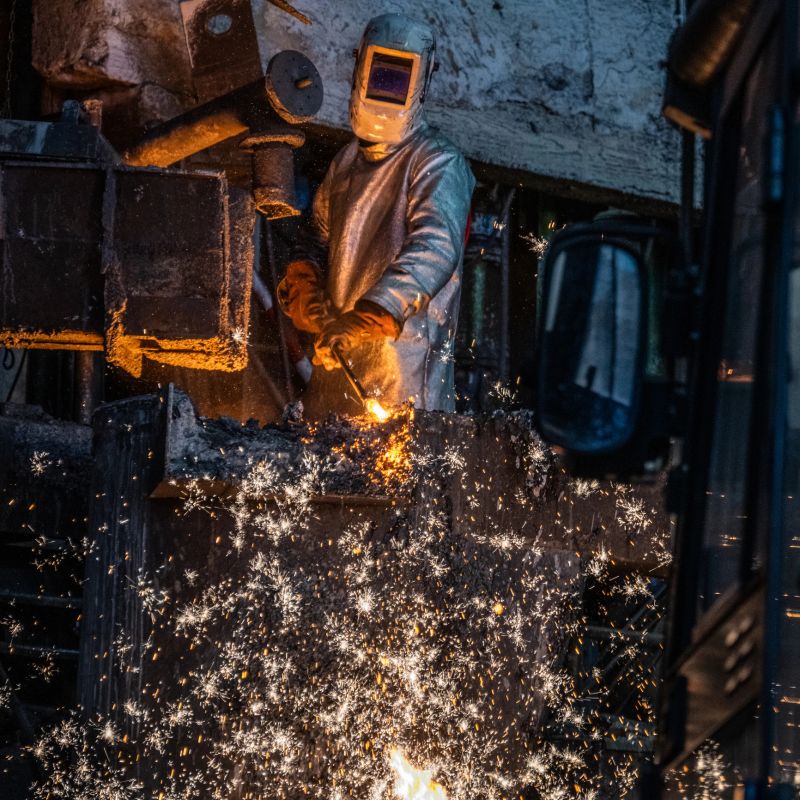 Metal worker in protective workwear discharging molten metal in a foundry.