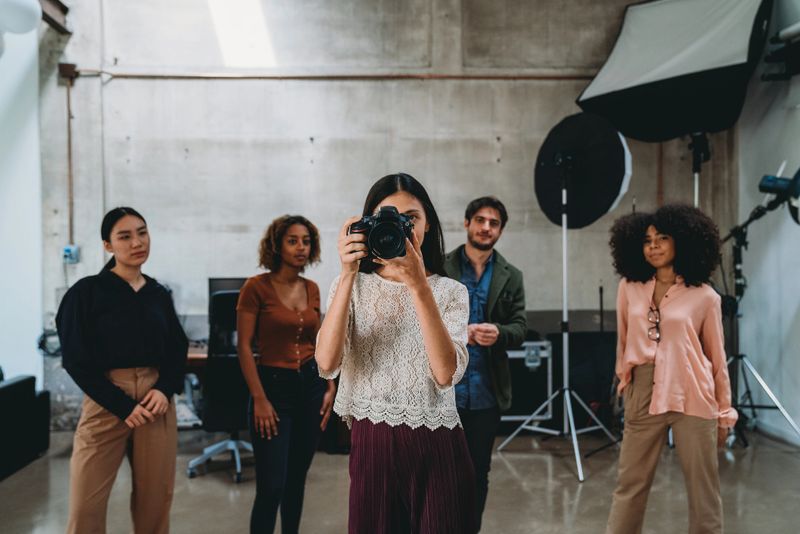 A woman photographer in her studio with a camera. People in the background.