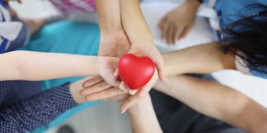 Hands holding a red heart together.