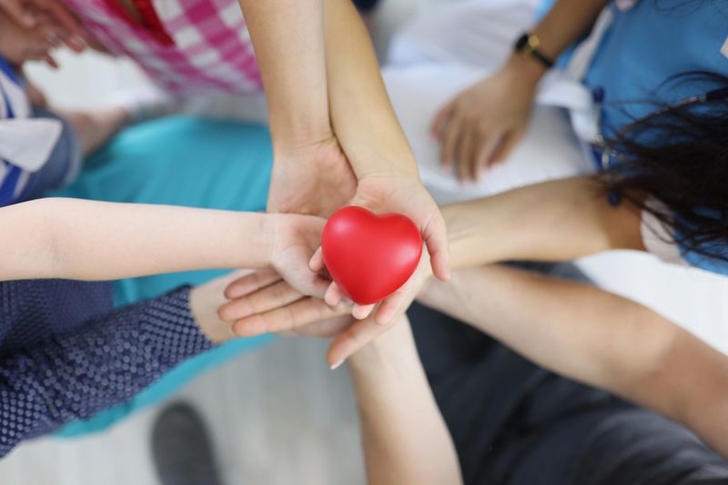 Top view of group of people holding red heart in hands. Adults and children support charity, health insurance, love, international cardiology day, heart health, donation, wellbeing concept