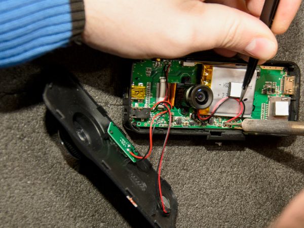 Person repairing a small electronic device circuit board with tools.