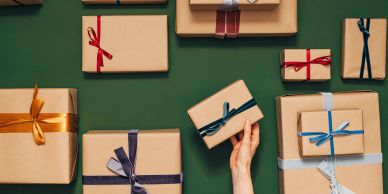 Hand holding a gift box with other wrapped presents on a green surface.