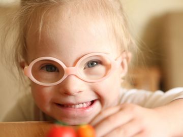 Smiling child with pink glasses looking at the camera.