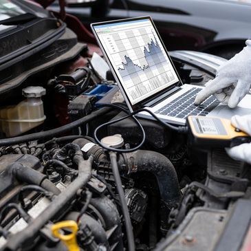 Mechanic diagnosing car engine with laptop and diagnostic tool.