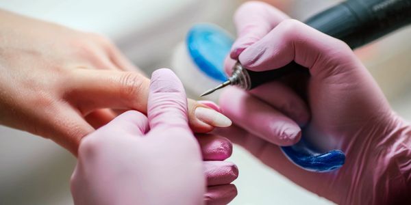 Nail technician wearing pink gloves shaping nails with an electric file.