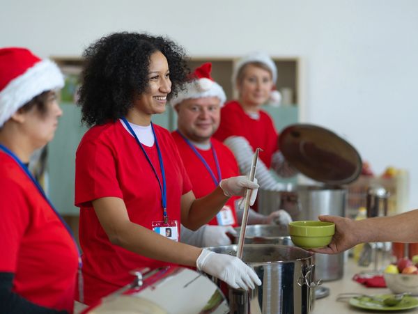 Volunteers in red shirts and Santa hats serving food during a holiday event.