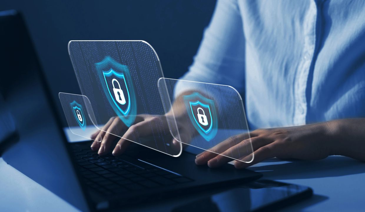 Person typing on laptop with digital security shields floating above keyboard.