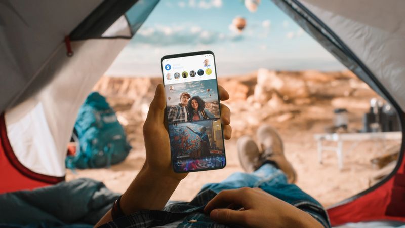 POV of a Tourist Vertically Holding a Smartphone and Checking Social Network Feed, Friends Latest Photos. Traveller Resting in a Tent on Top of a Rocky Mountain and Flying Hot Air Balloons