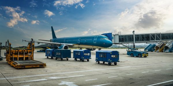 Airplane parked at airport gate with cargo carts nearby.