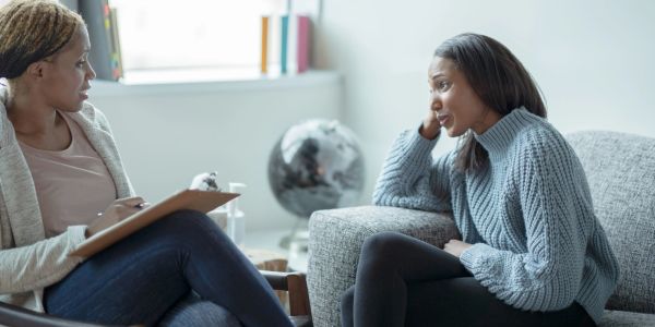 A woman talking to her therapist while the therapist has a clipboard on her lap and a pen in her han