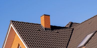 Modern house with a dark tiled roof and a brick chimney under a clear blue sky.
