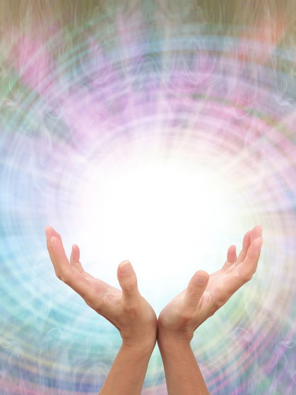 Hands reaching towards radiant white and colourful energy.