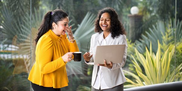 Two women laughing and enjoying a moment with a laptop and coffee indoors.