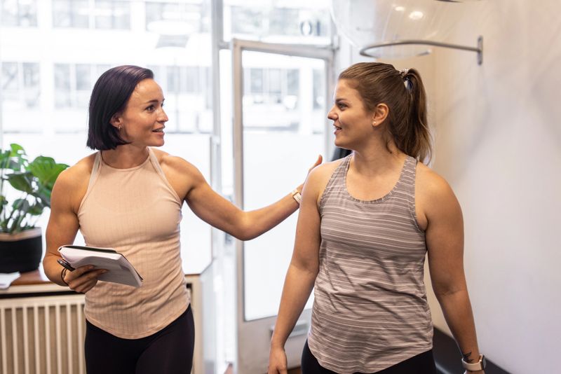 Fitness instructor talking with a woman student. Woman with personal trainer walking in fitness studio and talking.