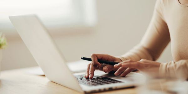 Person typing on a laptop with a pen in hand.