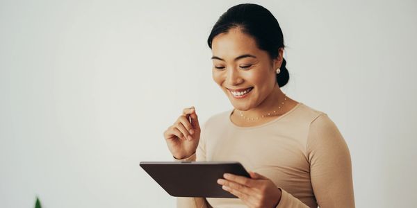 Smiling woman using a tablet against a plain background.