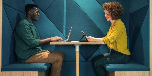Two colleagues working happily in a modern office booth.