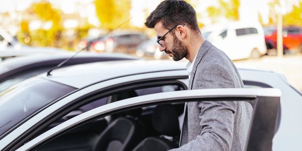 Man wearing glasses and a gray jacket opening car door to enter.