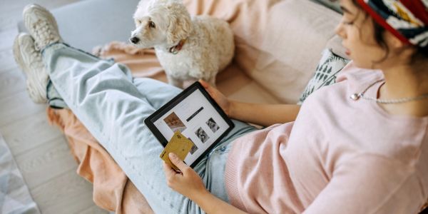 Woman shopping online with a tablet and credit card, dog beside her.