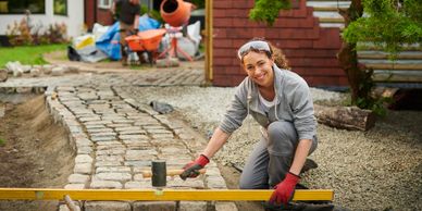 Woman working on a stone pathway, smiling at the camera.
