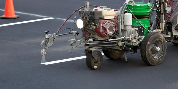 Machine painting white lines on a freshly paved road.