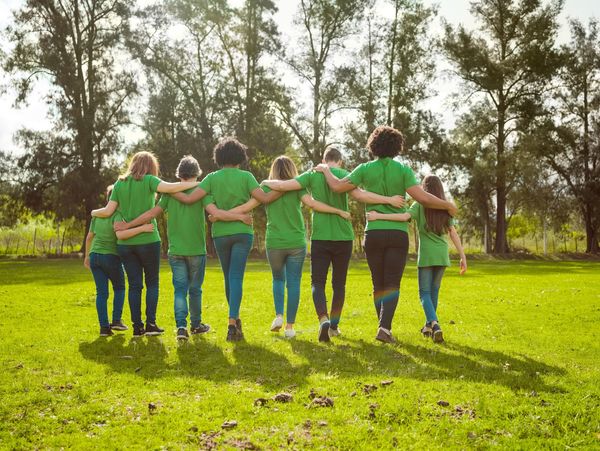 Group of people in green shirts walking arm-in-arm in a sunny park.