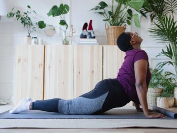 Person doing the upward facing dog yoga stretch in-home surrounded by plants.