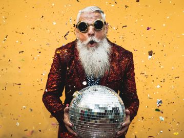 Elderly man with a long white beard holding a disco ball amid confetti.