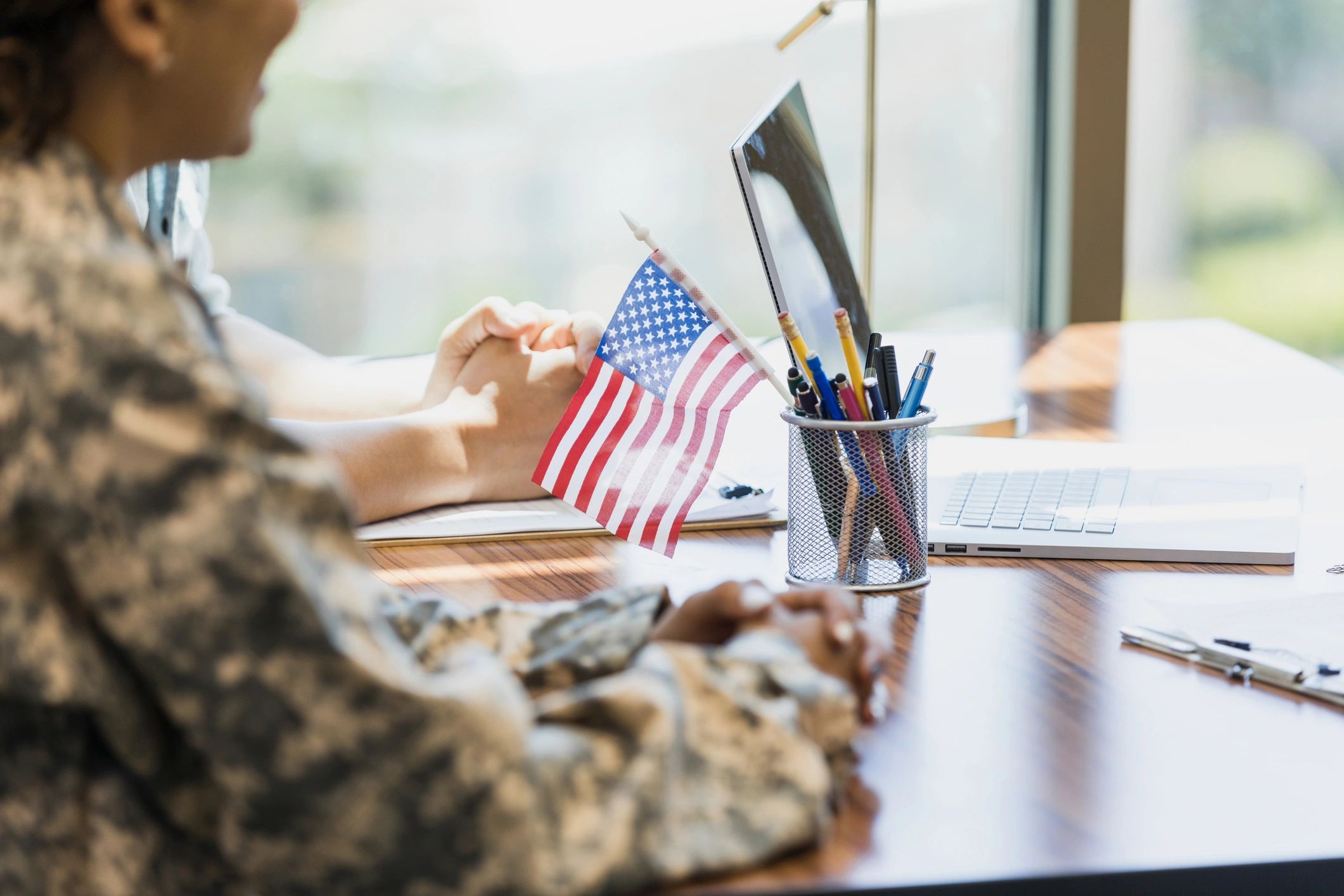 Military personnel in uniform near a laptop with a small American flag on the desk.