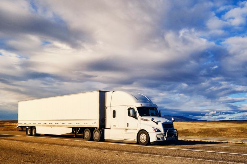 Large semi truck hauling freight on the open highway in the western USA under an evening sky.