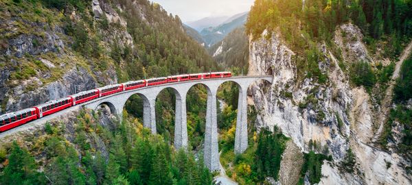 A scenic train winds through a mountainous forest landscape.