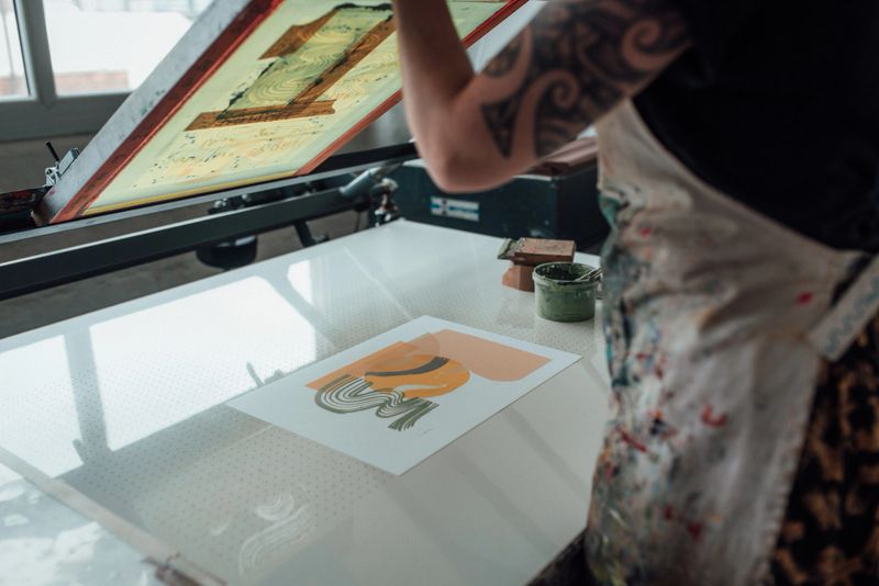 Artist lifting printing press to reveal freshily made print