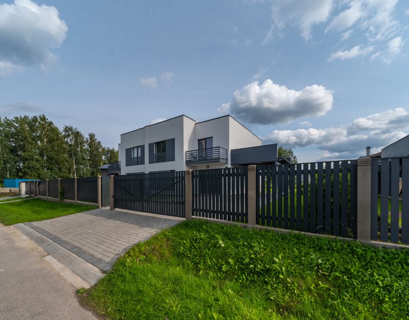 Modern exterior of luxury private house. External fence. Sunny day. Blue sky. Green lawn. Main entrance.