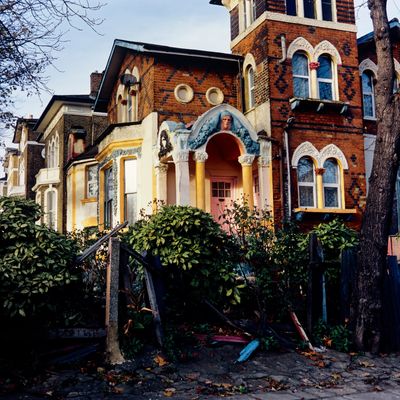 Old brick house with intricate arches and a broken fence in front.