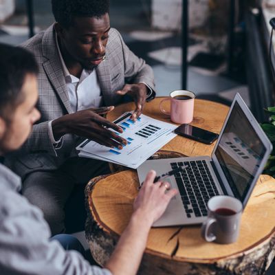 Two men discussing business charts and working on a laptop at a wooden table.
