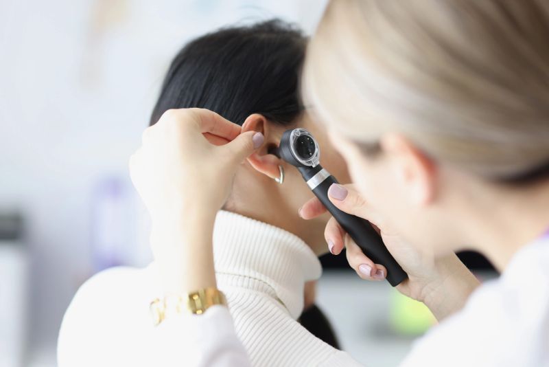 Close-up of female otolaryngologist examining ear with otoscope. Patient with earache at doctor appointment. Otolaryngology, medicine and healthcare concept
