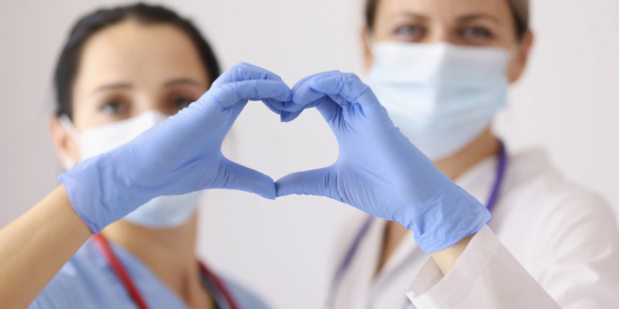 Two healthcare workers forming a heart with gloved hands.