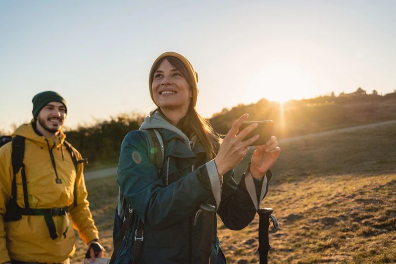Adventurous and happy woman, during her autumn hike with a boyfriend, taking photos of them and the nature with a mobile phone