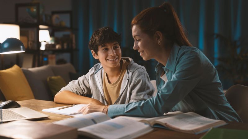 Young tutor helping a student with his homework, they are smiling at each other