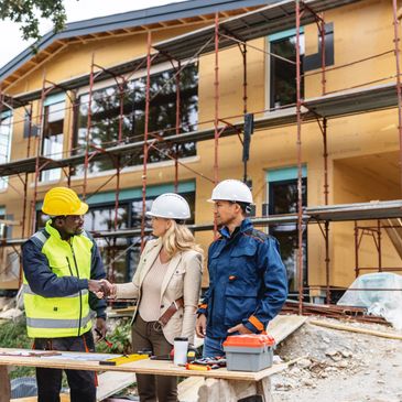 Three construction professionals shaking hands at a building site under construction.