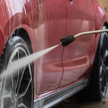 Pressure washing a red car's wheel and side panel.